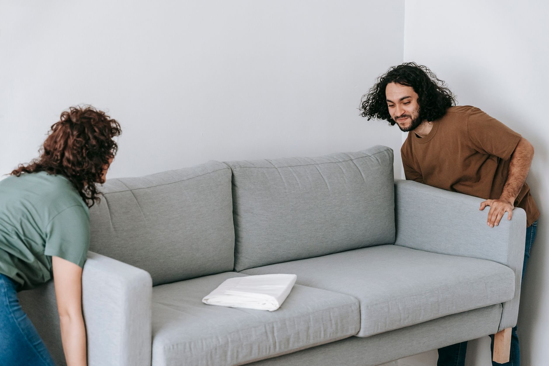 Two people carrying a gray couch out of a living room during a home cleanout